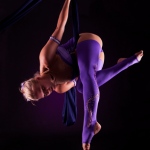 Aerial skills performer dances in midair as she spins herself around. 