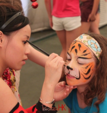 The face painter in Hong Kong is painting an amazing tiger face paint on a little lady face at a corporate festival event