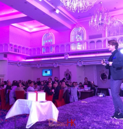 HK magician standing on a purple stage performing his stage act with the mobile borrow from the audience at a corporate annual dinner
