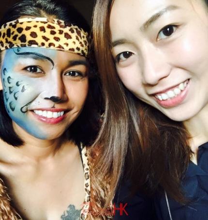 A face painter in HK taking picture with her at a juggle themed corporate event after she painted a blue and white leopard half face paint for her.