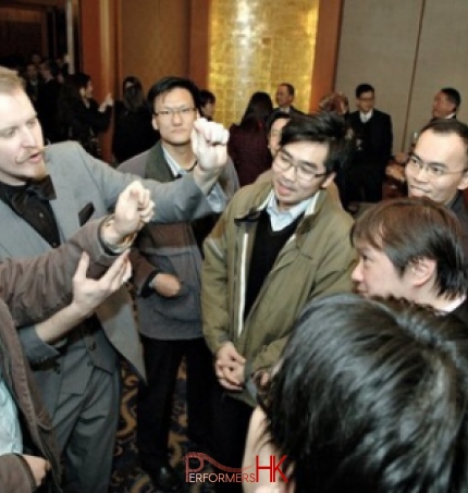 Roving Magician performing invisible coin magic with a audience at corporate cocktails party 