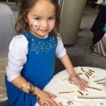 A little child having temporary henna tattoos on her both hands and face at a kids birthday party