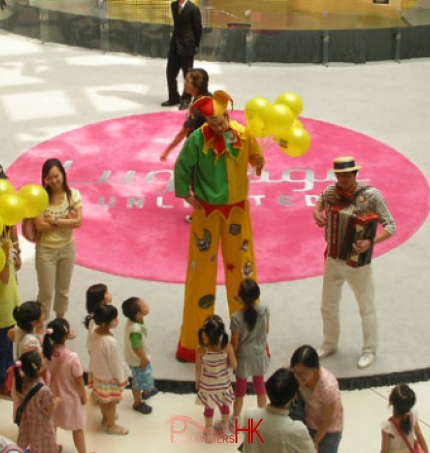 The stile walker wearing a patch jester stilts costume ,giving balloons away to children at shopping mall event.