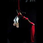 Female aerial performer hangs in midair by  wrapping herself around in silk clothes. 