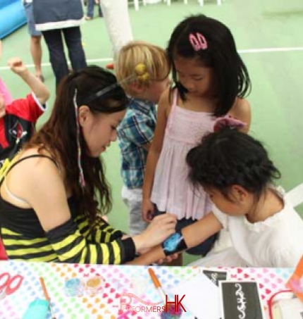 Face painter at a club in Hong Kong painting the arm of a child whilst sitting