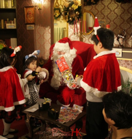 HK Santa performer giving out gift to three kids who wear reindeer accessories at a Kong Kong Christmas function. 