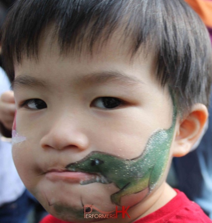 A professional face painter draw dinosaur face paint on a boys face at a  corporate kids function