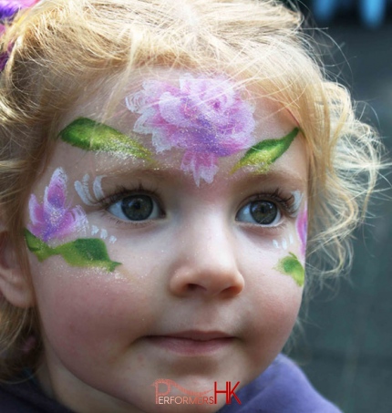 A face painter paint a white and purple flower face paint for a little girl at a school fair in HK 
