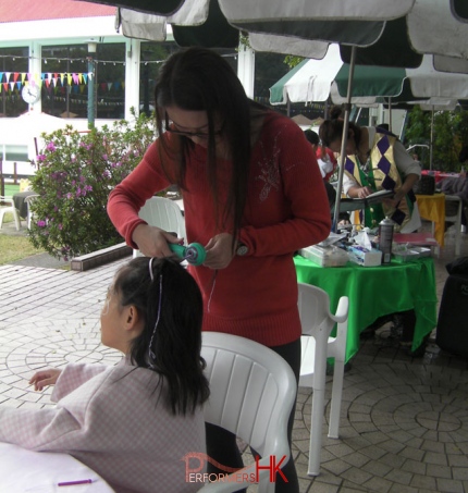 A professional staff using a a little string machine to braid a girls hair at a school fair in HK