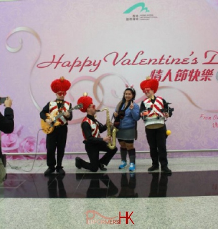 Three roving musicians dressed in red and white vests and love heart hats serenading a girl 