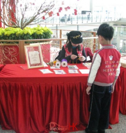 A female artist working on a Chinese knotting gift for child on a red table with the background of a flower pot at the Hong Kong Airport