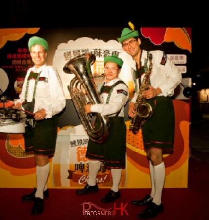 Three walk around musicians drum sax and tuba donning German attire and posing