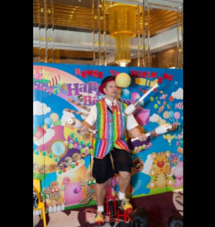 Juggler riding unicycle and juggling whilst spinning a ball in his mouth