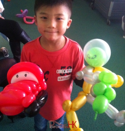 A Kid in HK posing with a McQueen and an Alien balloon , looks impressed by the roving balloonists skill at a corporate family event in AMC