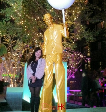 Golden stilt walker holding huge chupa chup and posing for picture with a lady