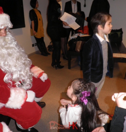 A westerner performer in Hong Kong dress as Santa , talking to a kid at a company Xmas party.