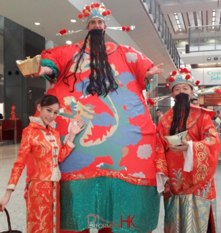 Stilt walker wearing giant inflatable Choi Sun costume taking picture with Choi Sun and Choi Nui performer at HK airport Chinese New Year event