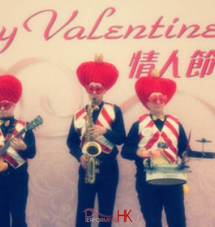 Three musicians wearing valentine day costumes with large love heart hat and red and white vests