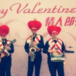 Three musicians wearing valentine day costumes with large love heart hat and red and white vests