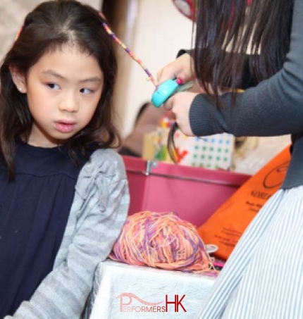A lady wrapping the girl hair to braid with a little string machine at a corporate children event