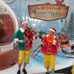 Three strolling musicians playing the violin drum and trombone at the HK Airport nest to santa in a globe 