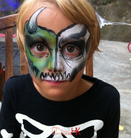 Face painter draw a skull face painting on a kid to match his costume at a Halloween function in Hong Kong