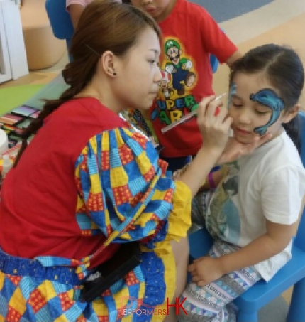 Face painter in HK very focused, drawing a dolphin face paint on a child at a school event