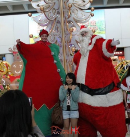 two giant stilt charatcer walk around at christmas hong kong airport in front of a white christmas tree