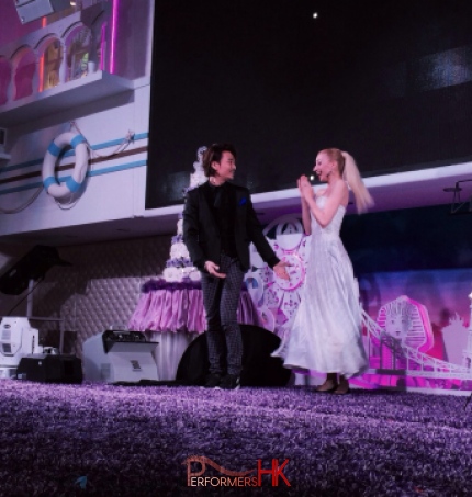 Magician in Hong Kong standing on the stage ,performing stage magic with is assistant and change her dress from blue to white at a corporate event