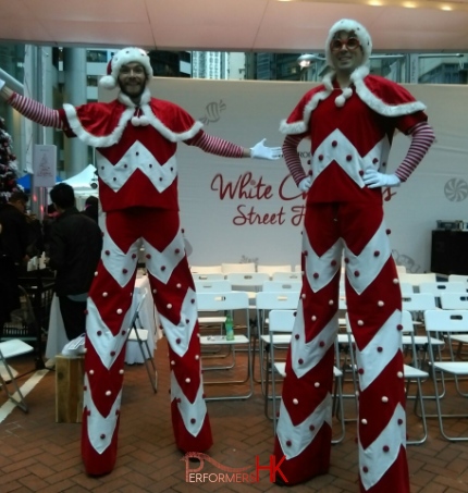 Two candy cane looking stilt walkers standing next to Swire stage