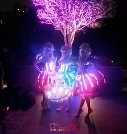 The LED dancers donning period dresses standing under lit up tree