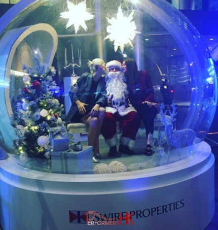 Two girls kissing santa inside a giant snow globe