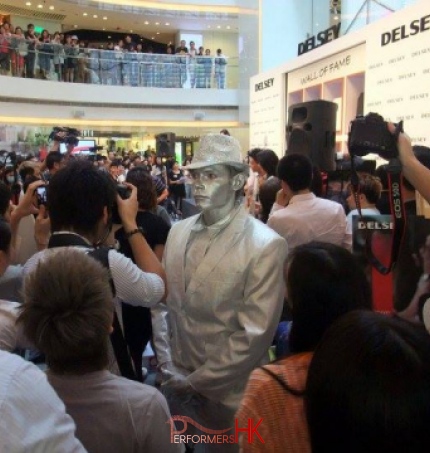 Silver man human statue standing in a crowd with lots of photographs being taken 