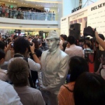 Silver man human statue standing very still as much as humanly possible with photographers in front. 