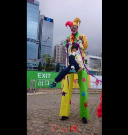 Stilt-walker lifting up a child with a tall Hong Kong building in the background