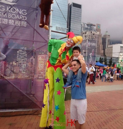 Stiltwalk wearing jester costume taking photo with dad with child on shoulders