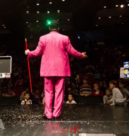 Children looking at the magician in Hong Kong who holding a red wand , standing next to the magic case , performing at the corporate kids event 