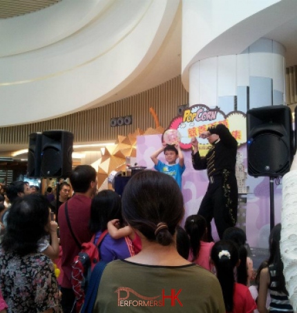 Magician in HK performing needle through a balloon magic trick on stage with a child audience on stage at Popcorn mall
