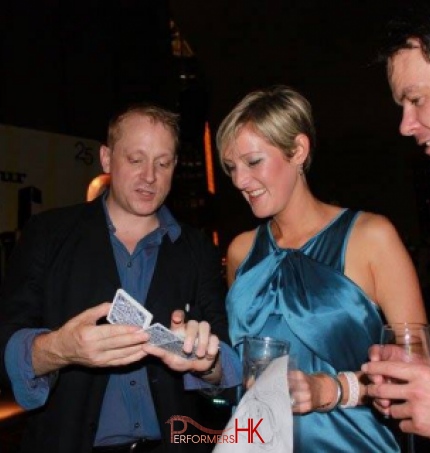 Magician playing with cards to two guests holding drinks 