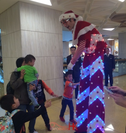 Led stilt performer shaking hands with young child in a shopping mall in Hong Kong
