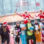 Two Xmas red and white stilt walkers standing behind a group of animal costume models