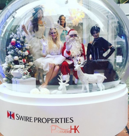 Giant snow globe with santa and three models dressed as christmas angels inside.