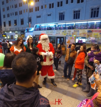 HK models and performer dress as Santa ,Santa girl and Elf standing outside Hong Kong greeting and photo taking with the guests at a Christmas corporate event.