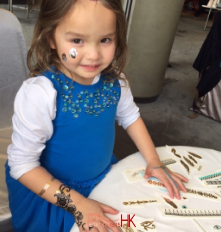 A little child having temporary henna tattoos on her both hands and face at a kids birthday party