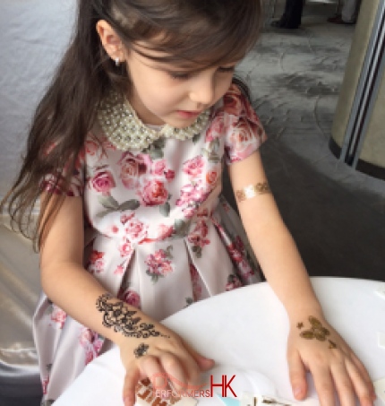 Little girl having three temporary henna tattoos on her both hands at a corporate party