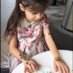 Little girl having three temporary henna tattoos on her both hands at a corporate party