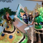 Dancers and drummer in bright green and white costumes.