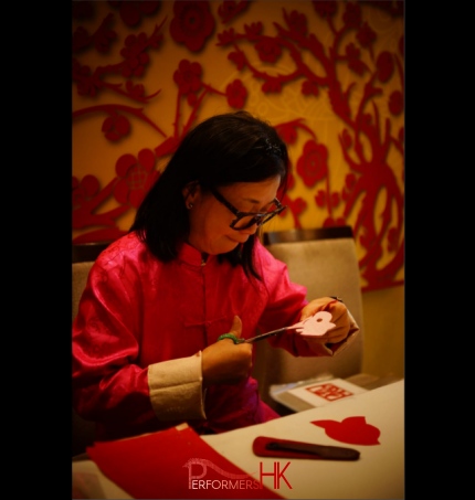 wearing pink traditonal chinese costume, artist is working on a cut out for guests