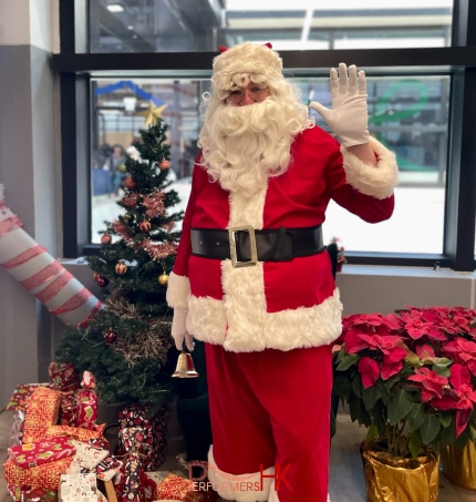Santa in red suit in front of a christmas tree