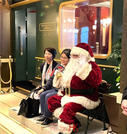 Santa Pete at Peninsula hotel front of a green train on a bench taking photo with guests